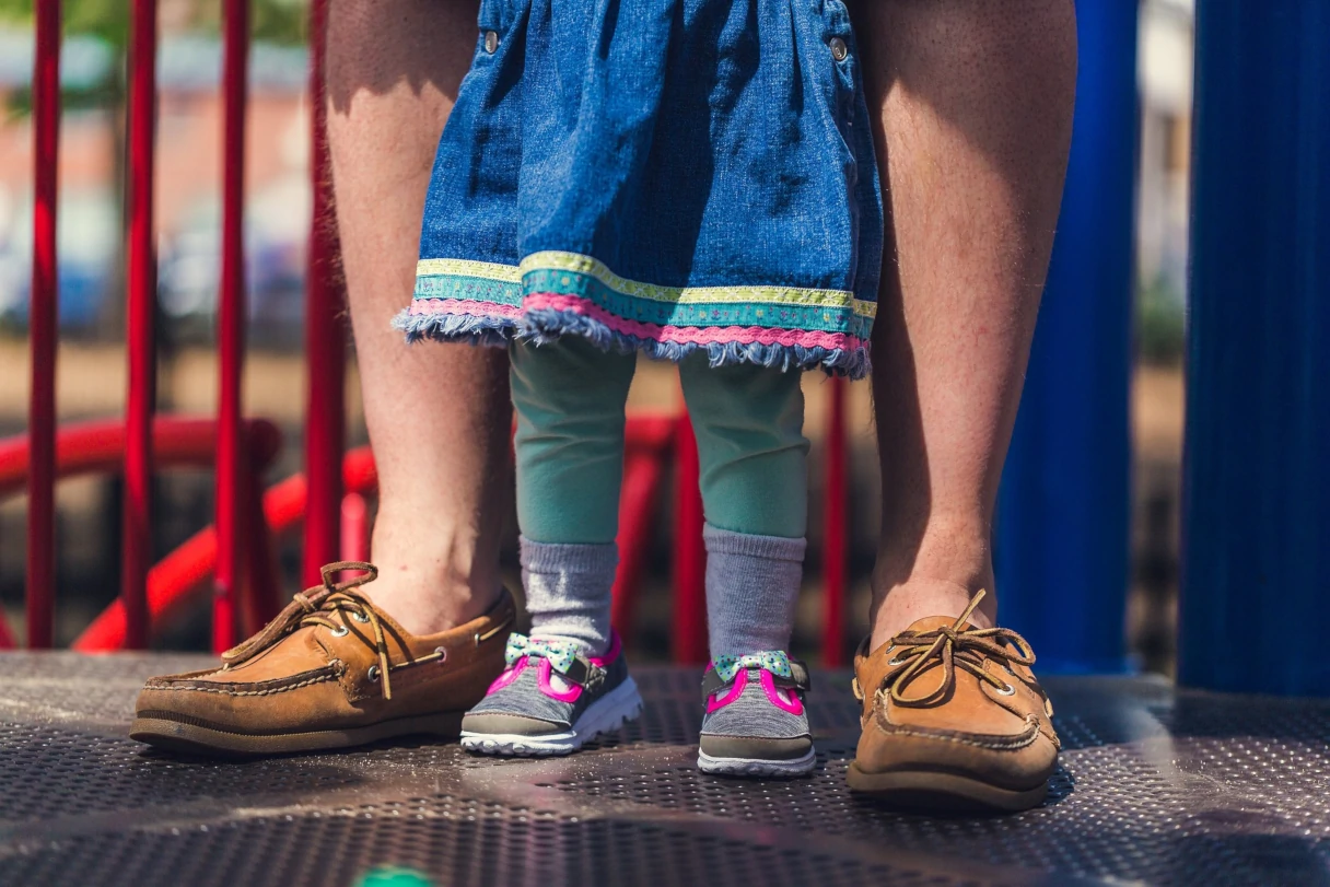 Father and daughter standing side by side, legs, playground
