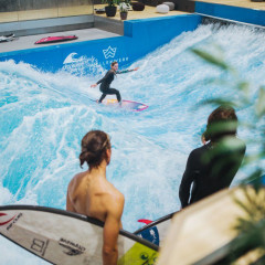 Valeska Schneider ist in den Wellen auf ihrem Becken auf der Welle. Andere Surfer stehen am Beckenrand und schauen zu.