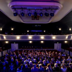 Saal des Kabaretts Die Distel. Mit Menschen gefüllter Saal, lila Saallicht.