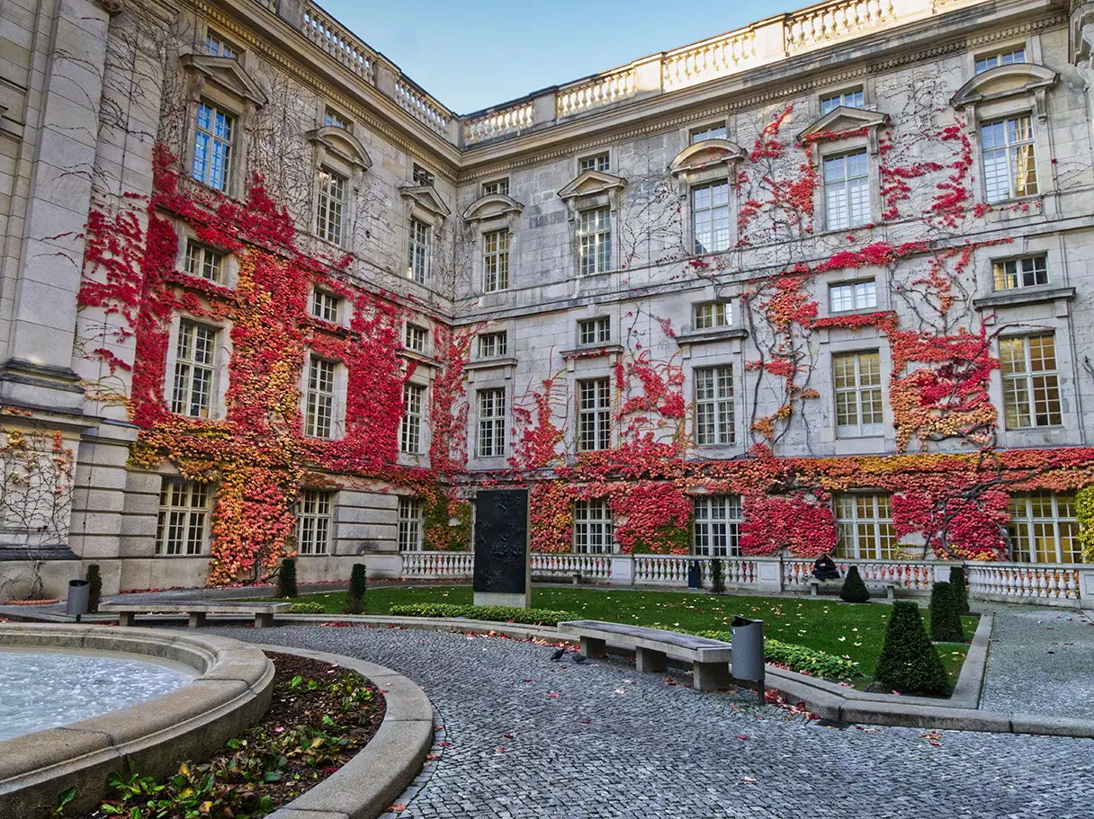 Staatsbibliothek Unter den Linden mit buntem Herbstlaub an der Fassade. Innenhof der Bibliothek. Ein Brunnen ist noch angeschnitten.