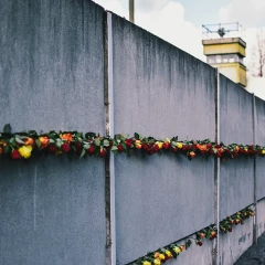 View of the Berlin Wall at the memorial in Bernauer Strasse. The Wall is decorated with red, yellow and orange roses. In the distance, you can see a border tower peeking over the Wall on the right edge of the picture.