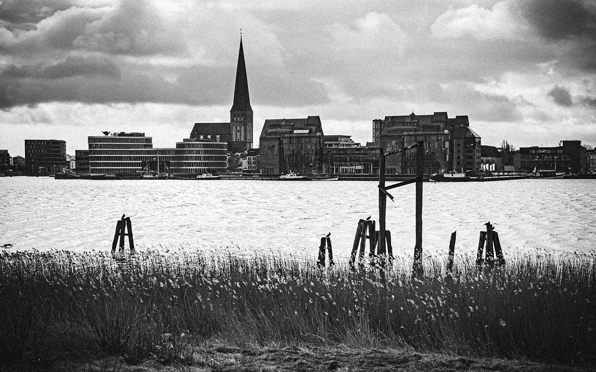 View of Rostock in black and white. You can see the church spire and a small skyline on the other side, with water between the viewer and the skyline.