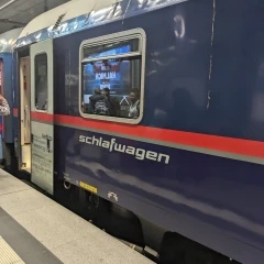 ÖBB Nightjet, train is at the platform and the passengers can board, blue train with red stripe, lettering “Schlafwagen” can be read