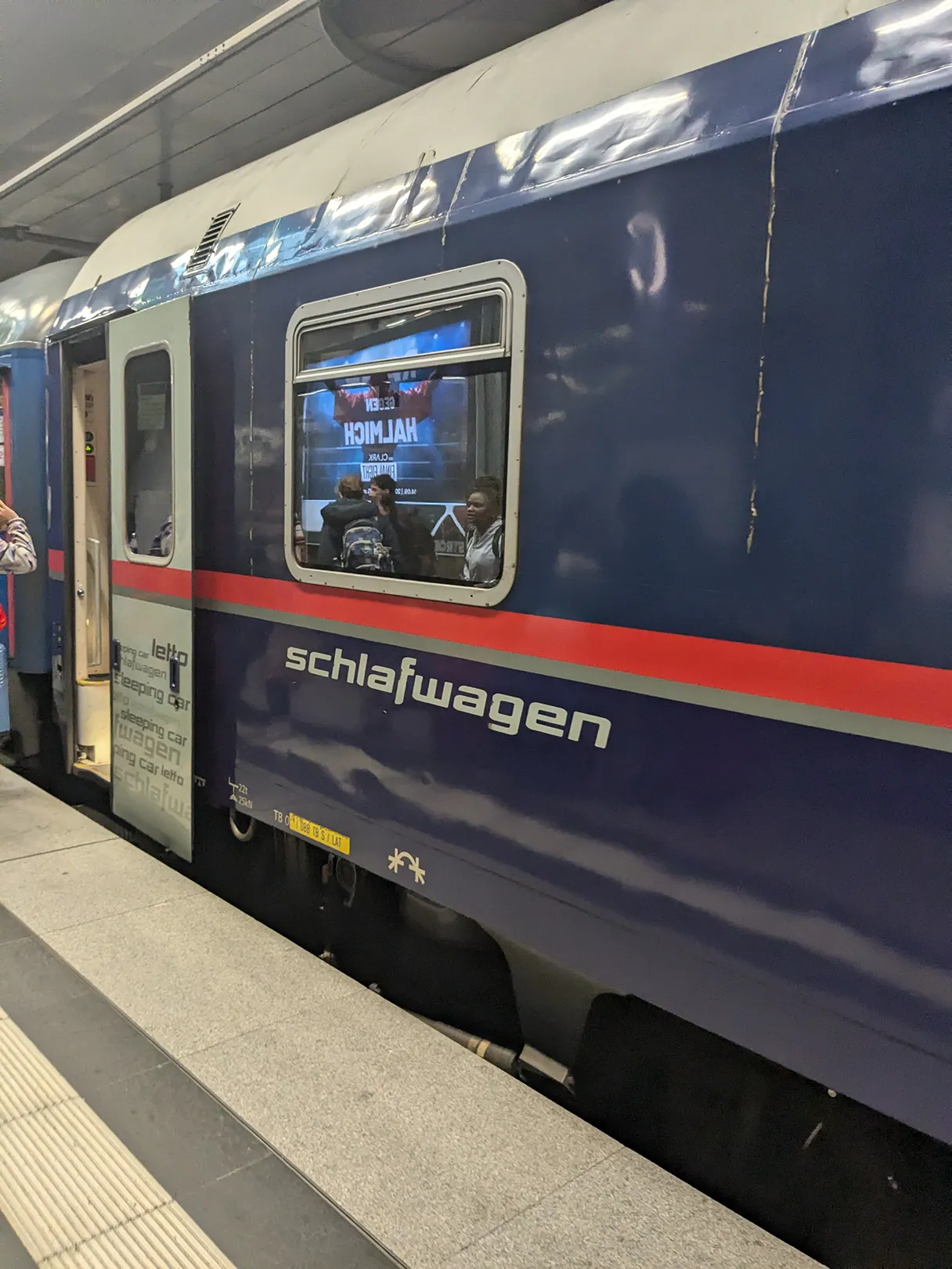 ÖBB Nightjet, train is at the platform and the passengers can board, blue train with red stripe, lettering “Schlafwagen” can be read