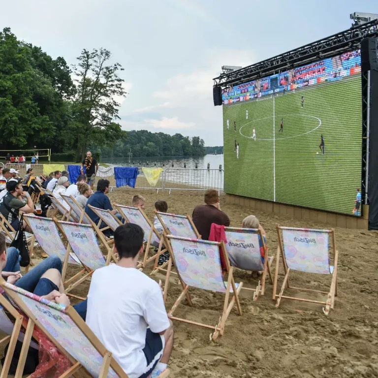 Strandbad Wendenschloß, Leinwand, Liegestühle stehen im Sand, Fußballspiel läuft