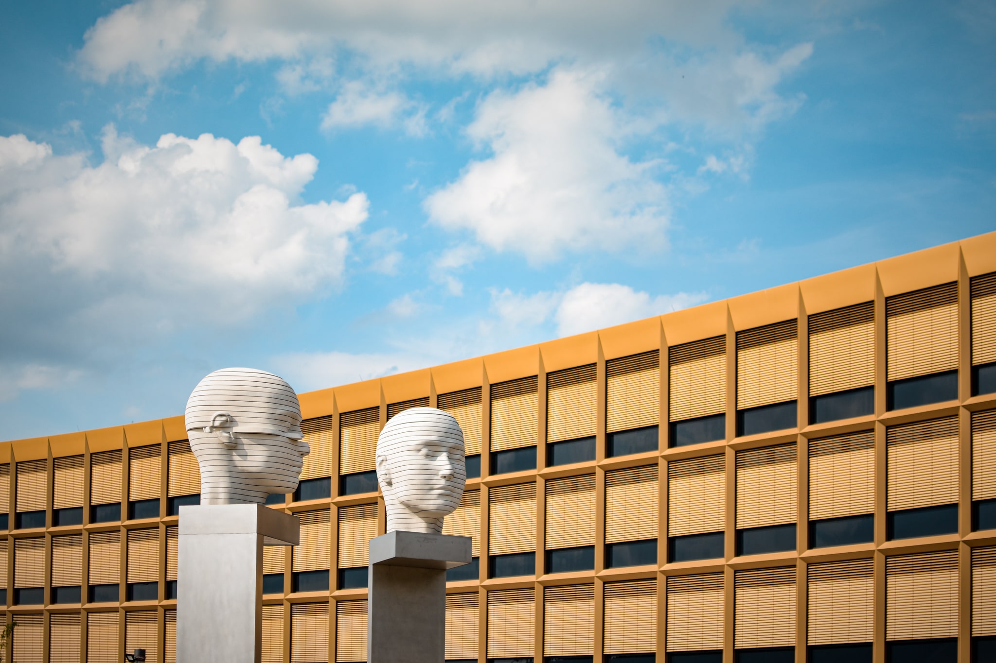 two white heads sculptures, orange house with many windows, blue sky, sunshine