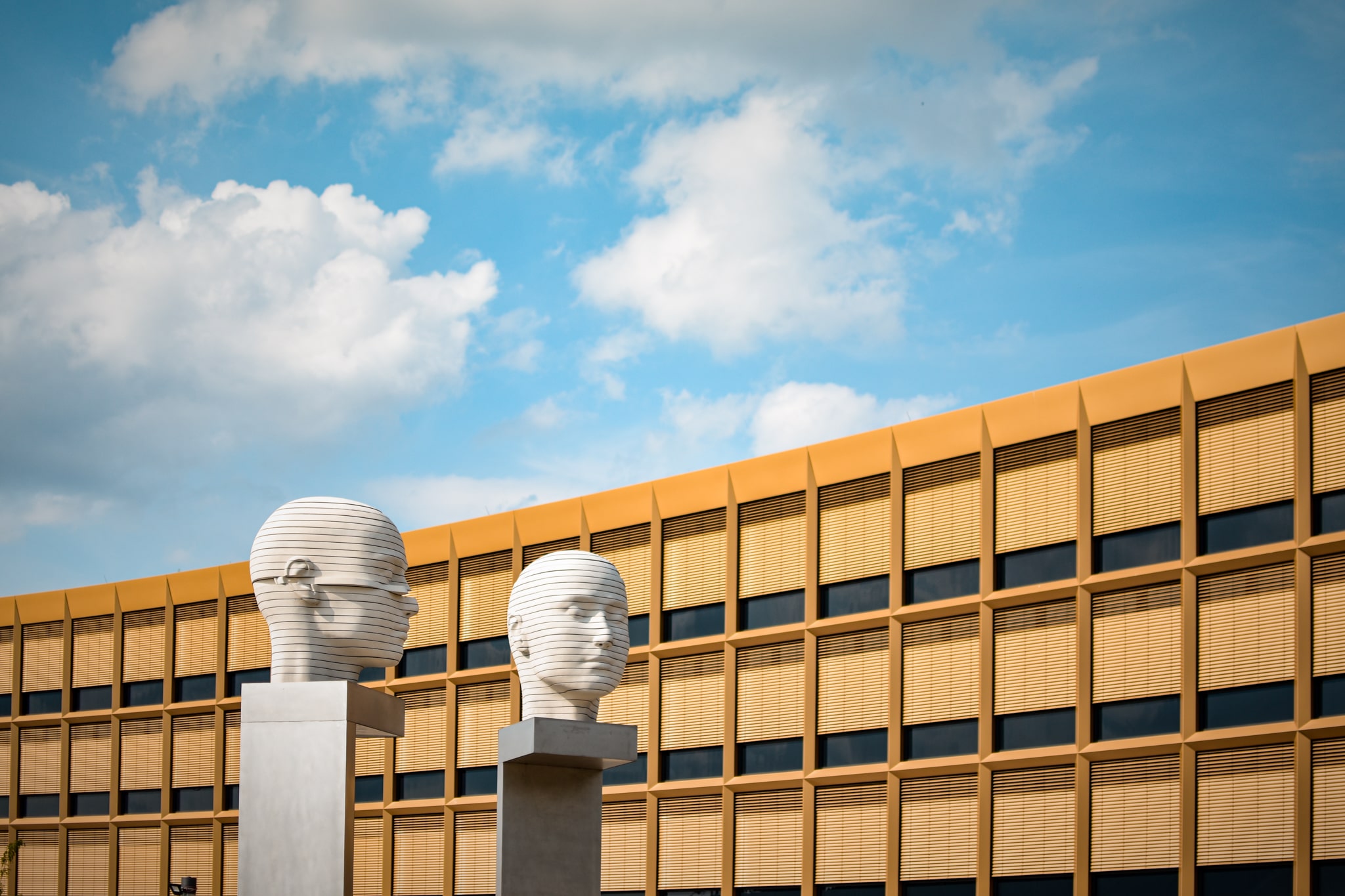 zwei weiße Köpfe Skulpturen, orangenes Haus mit vielen Fenstern, blauer Himmel, Sonnenschein