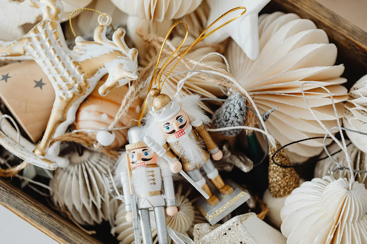 View from above into a box full of bright Christmas decorations. Two white nutcrackers and paper umbrellas in various sizes are lying around.