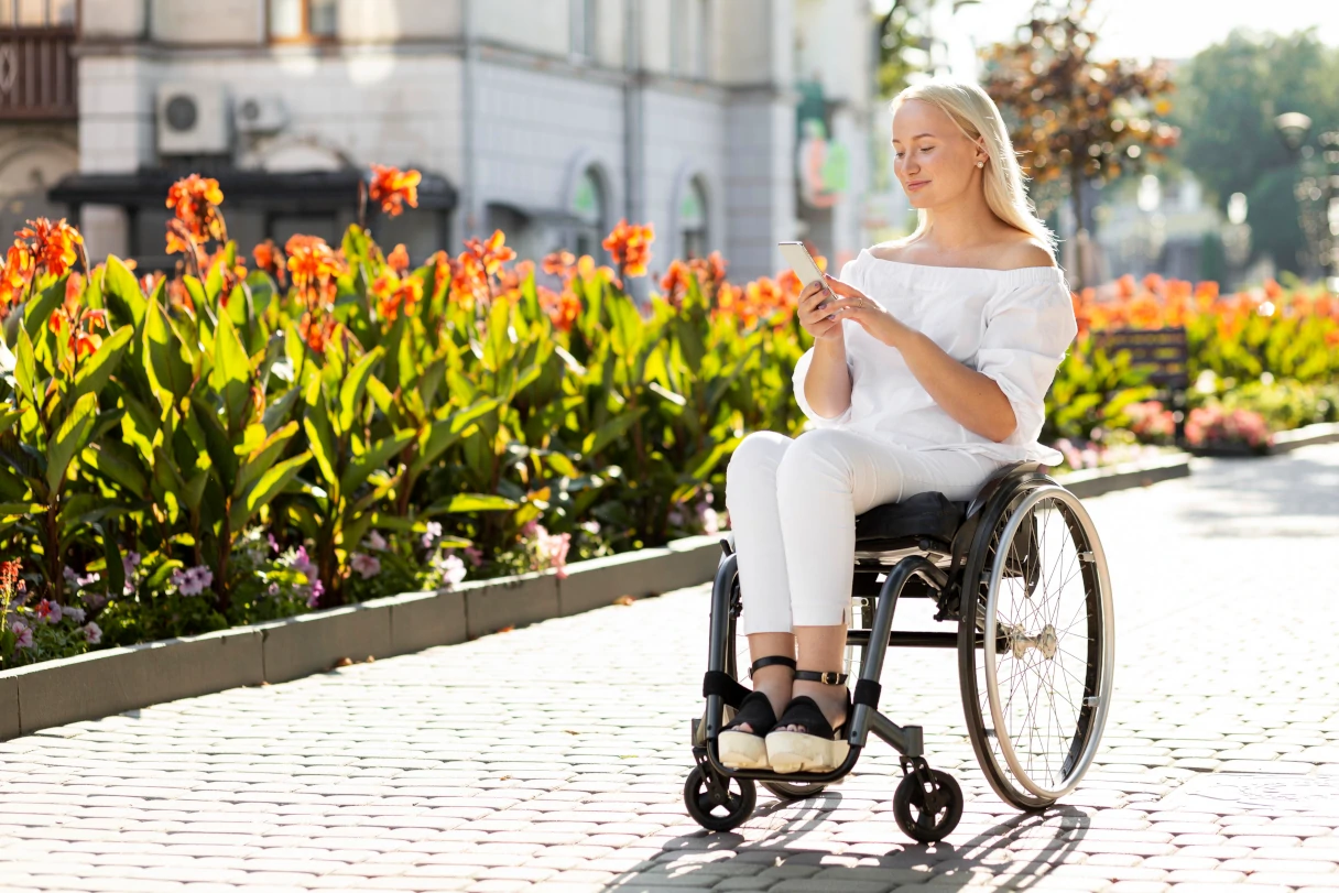 Woman in a wheelchair in front of a green flower border with red flowering plants