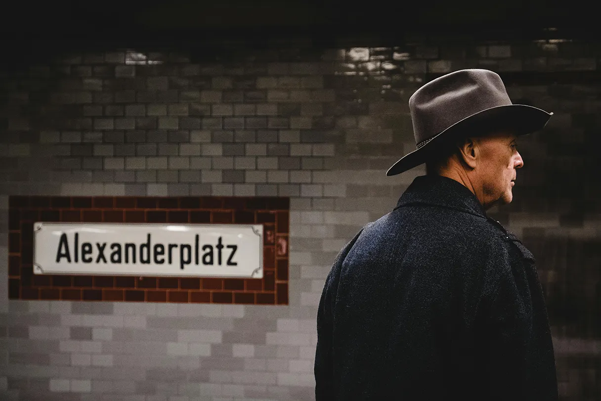 Mann mit Hut steht am Bahnsteig Alexanderplatz und wartet auf die U-Bahn, dunkle Atmosphäre