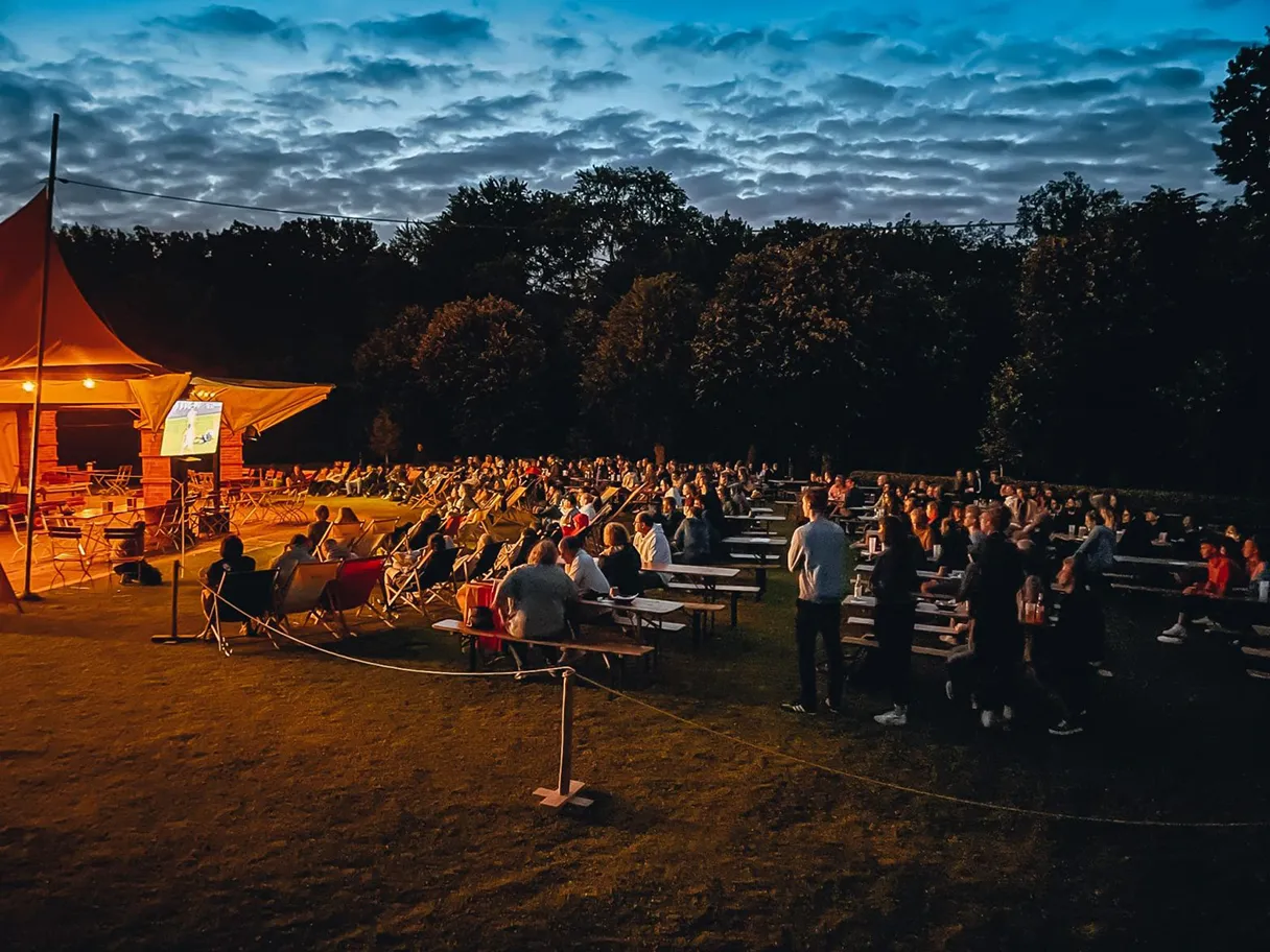 Waldhochseilgarten Jungfernheide, Sommergarten, Public Viewing, menschen sitzen dicht nebeneinander und schauen auf die große Leinwand