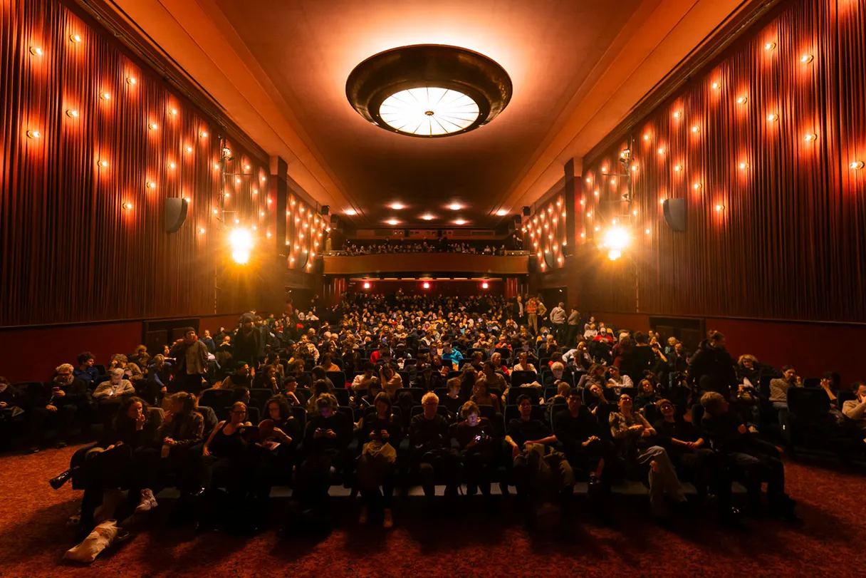 View of the packed movie theater at the Delphi-Filmpalast. Chandeliers on the ceiling, warm light.