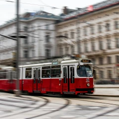 The red and white streetcar in Vienna crosses the street. The streetcar is in focus and the background is blurred, making the movement in the picture clearer.