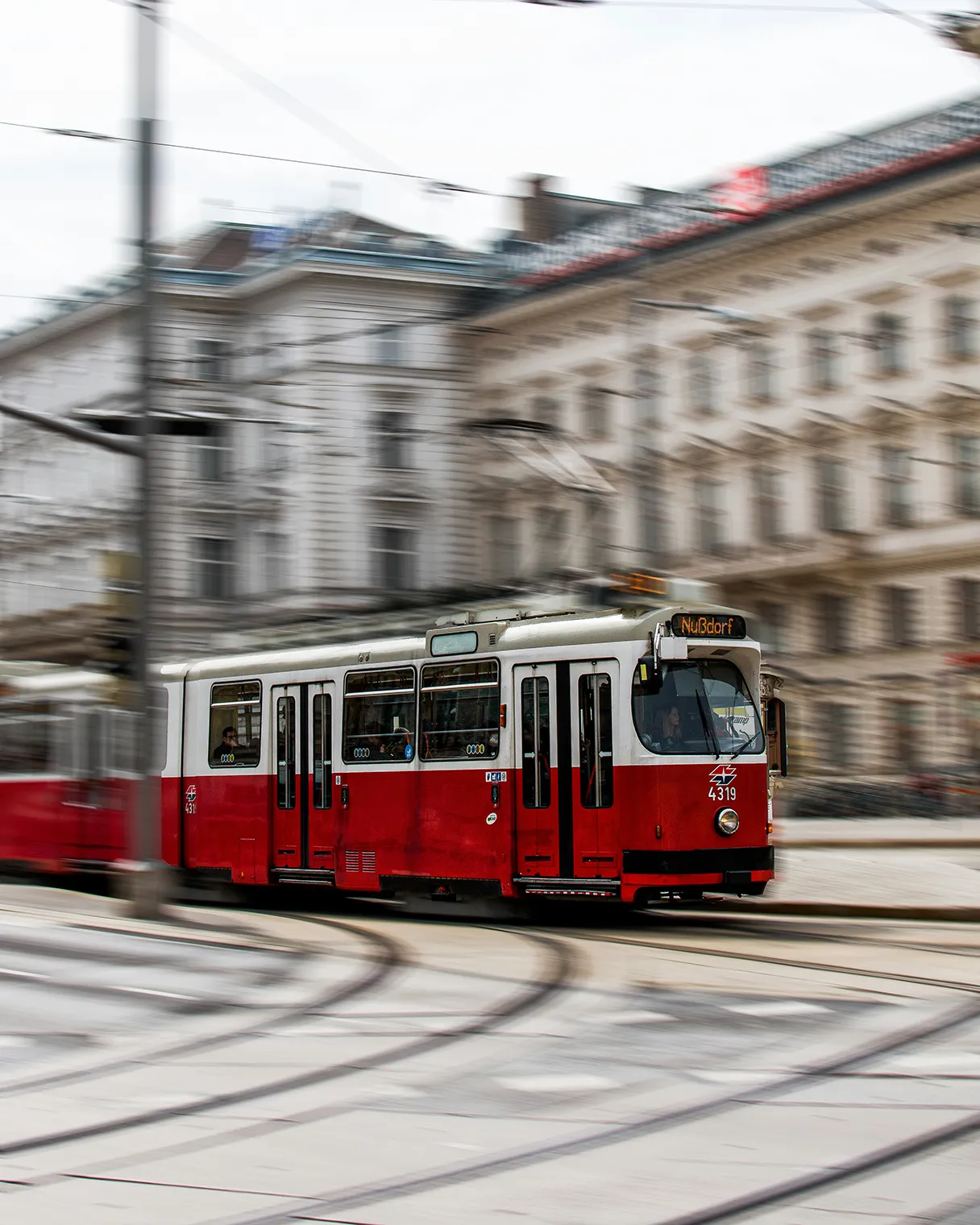 The red and white streetcar in Vienna crosses the street. The streetcar is in focus and the background is blurred, making the movement in the picture clearer.