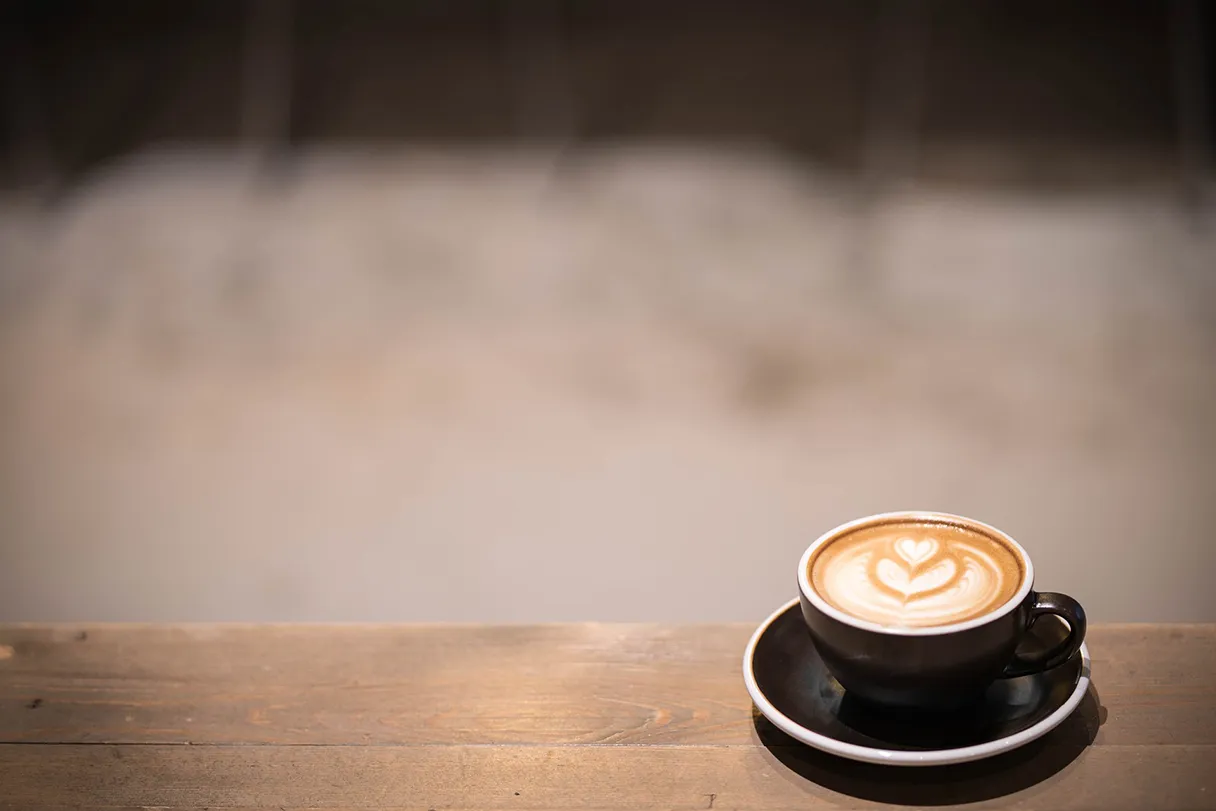 Coffee cup stands on a table, nothing else can be seen in the picture