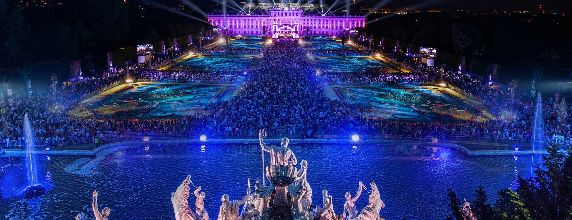 Summer night concert of the Vienna Philharmonic Orchestra, evening atmosphere, the palace garden is colorfully illuminated, guests stand in the palace garden