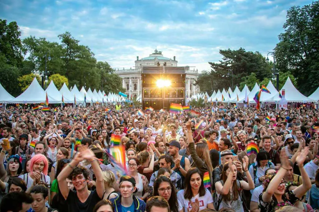 Pride Village Wien, Hintergrund Burgtheater, der Rathausplatz ist voll mit feiernden Menschen, Regenbogenfahen überall