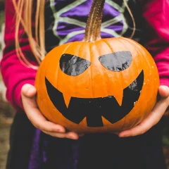 Girl holding a large pumpkin with a black face drawn on it, girl wearing a spider costume