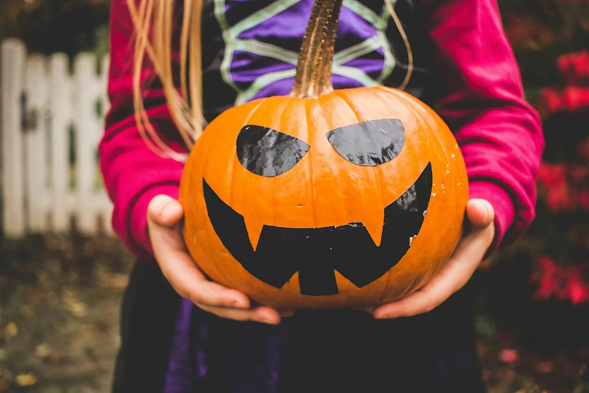 Girl holding a large pumpkin with a black face drawn on it, girl wearing a spider costume