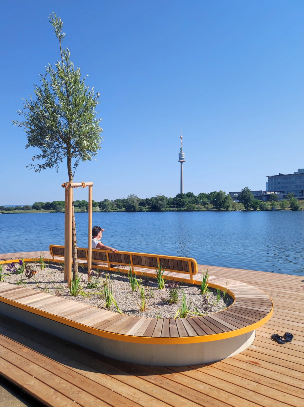 Donau, Flußufer, Frau sitzt auf einer Bank und schaut auf das blaue Wasser, Hintergrund Donauturm, blauer Himmel