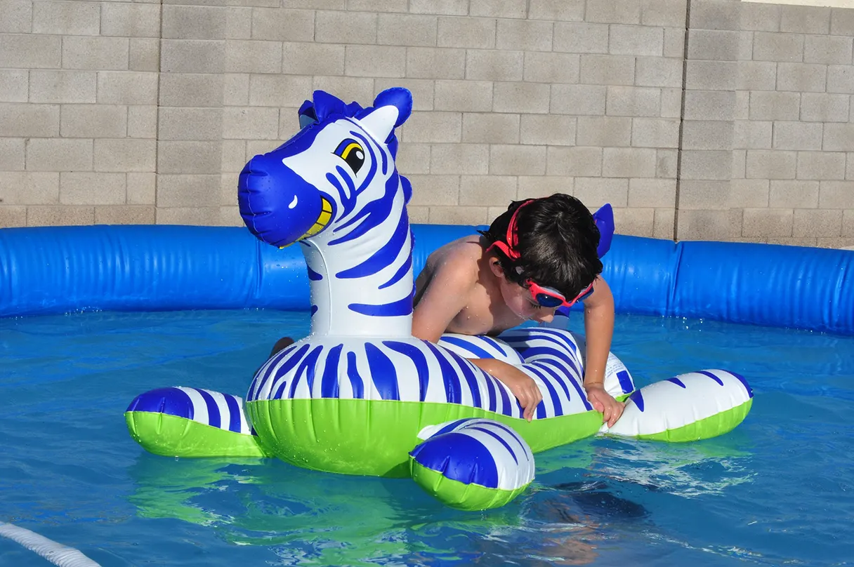 Little boy playing on an inflatable zebra in the swimming pool