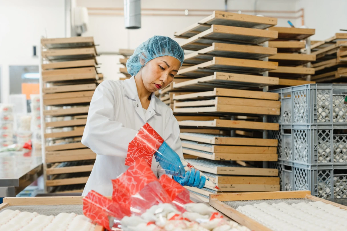 Aseli, Mitarbeiterin füllt die fertigen Schaummäuse in Tüten um, Blick in den Fabrikraum