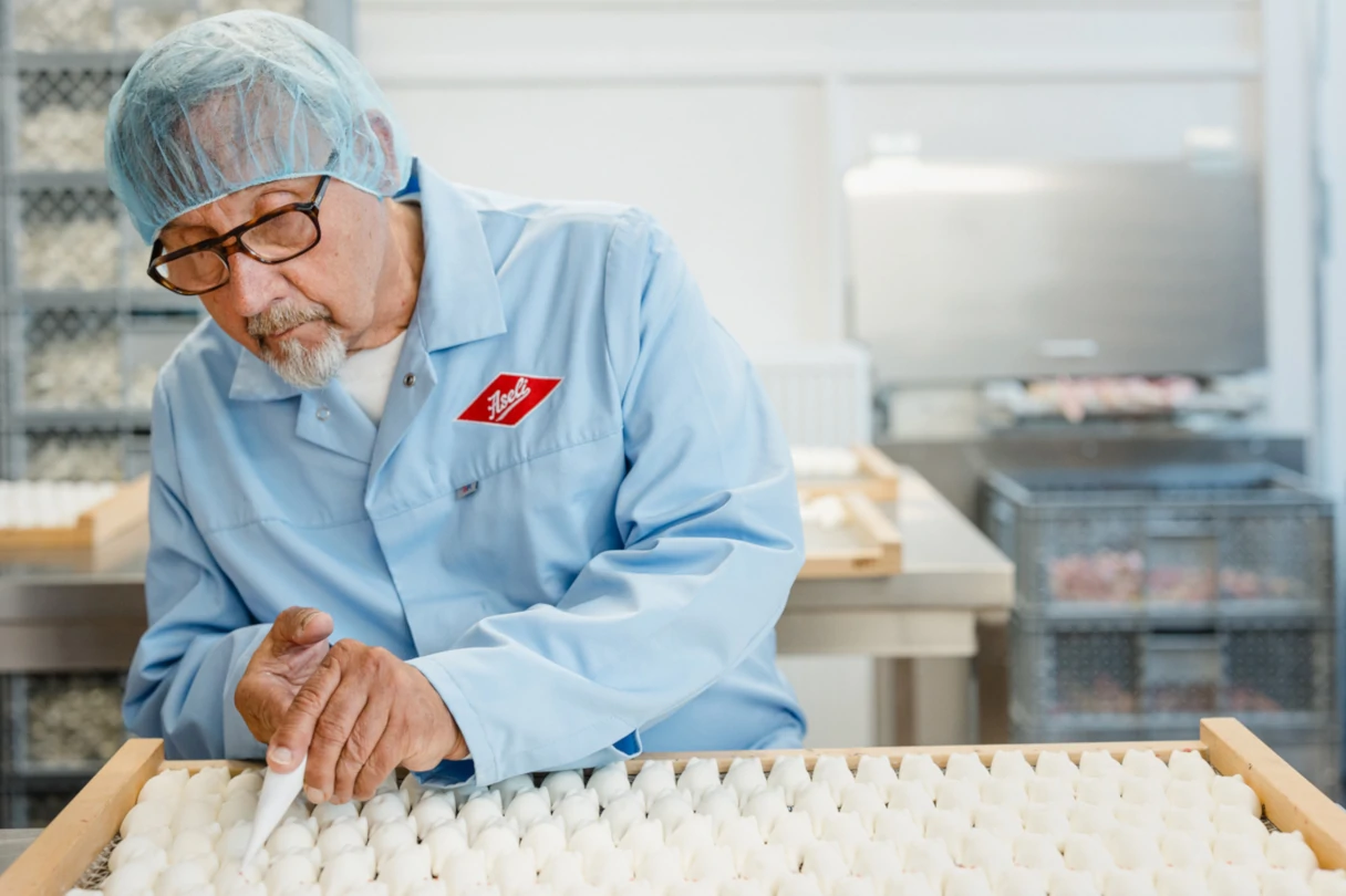 Aseli Manufaktur, Berlin, man in blue smock and transparent hairnet on his head decorates the white mice with black and red eyes