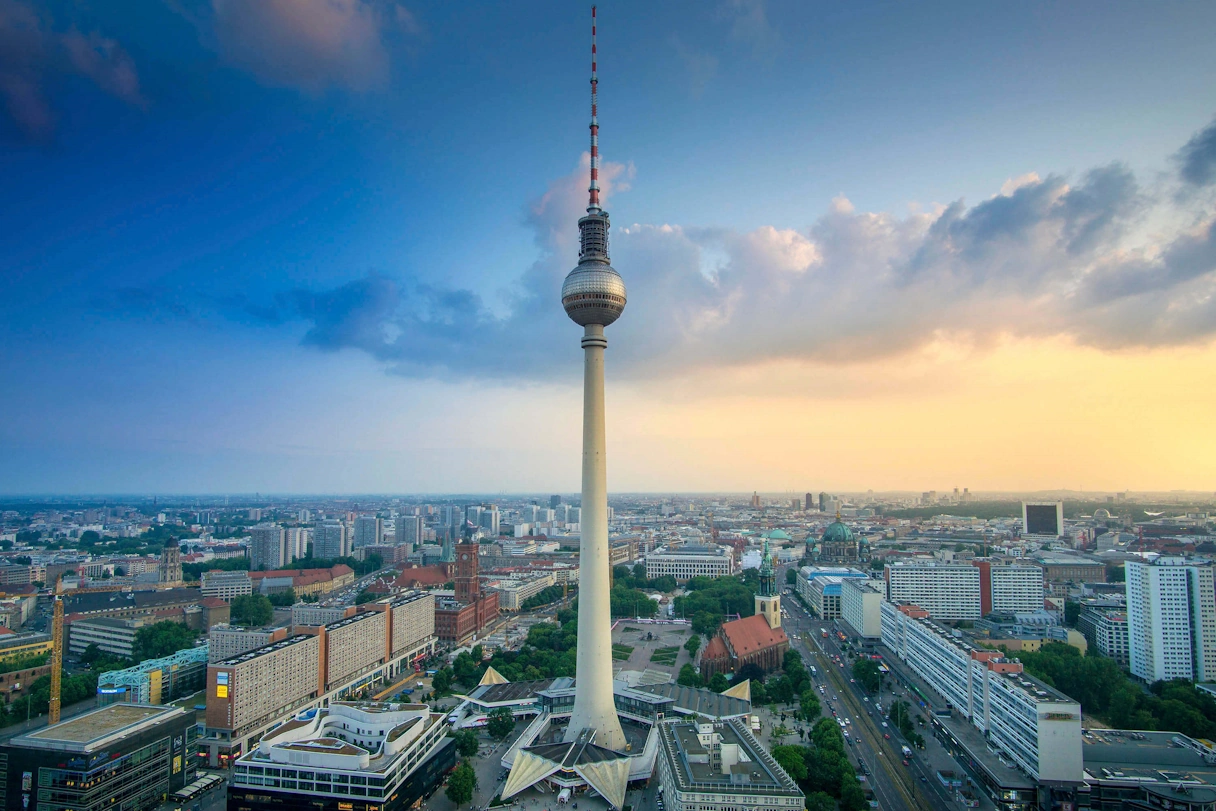 The Berlin television tower from above. The city and skyline can be seen around it. The sky is slightly cloudy