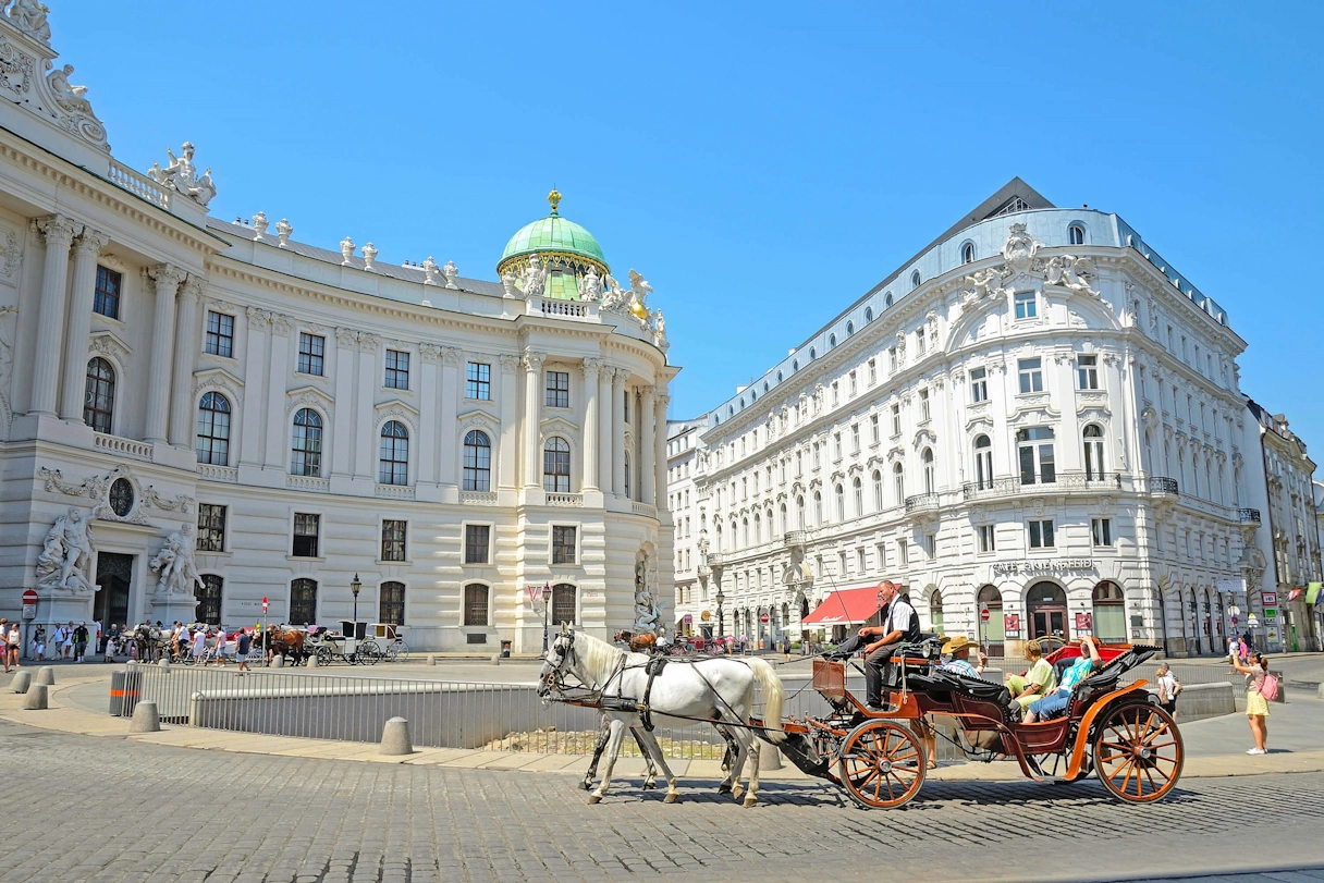 The Spanish Riding School in Vienna from the outside. In front of it are people and a carriage with two horses