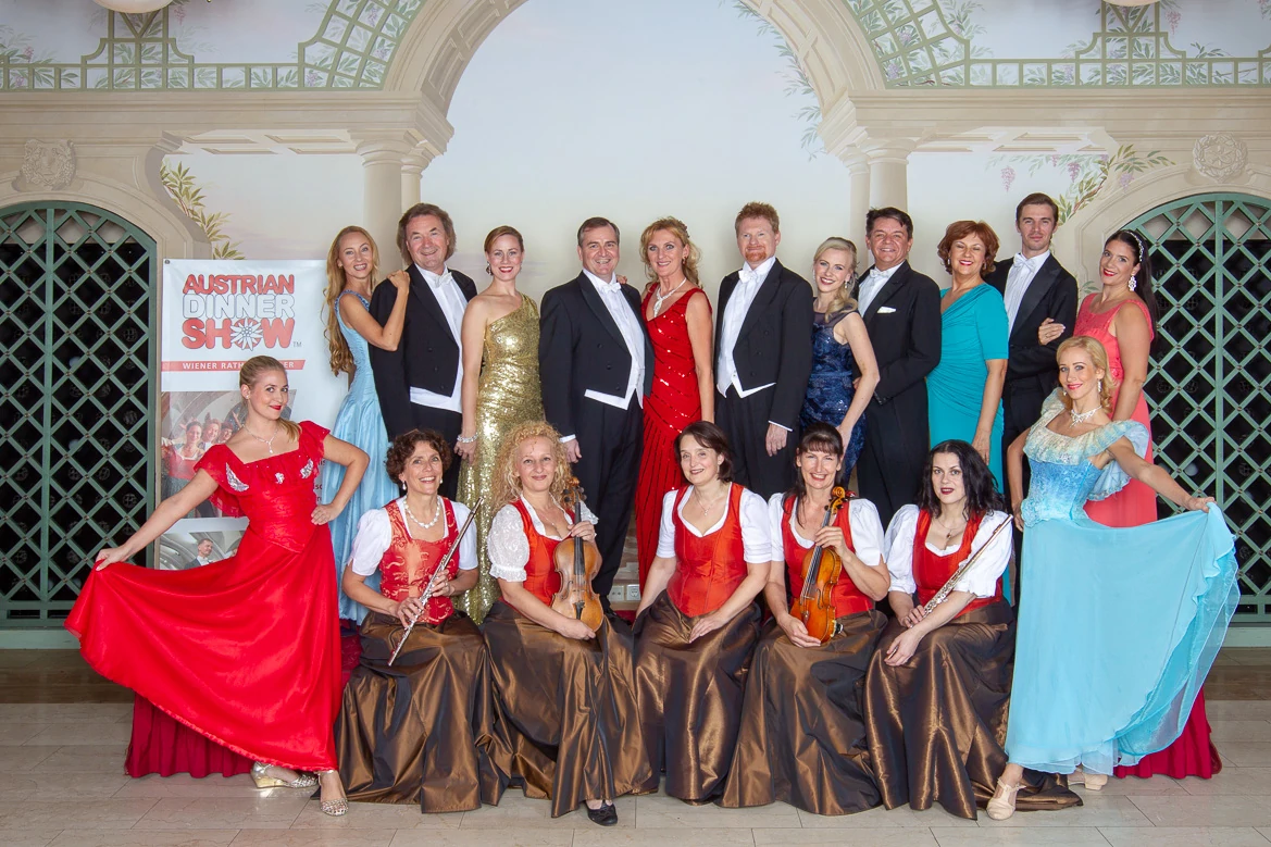 Austrian Dinner Show, Wien, Gruppenbild, Orchestermitglieder mit ihren Instrumenten, Sängerinnen in Abendkleidern und Sänger in schwarzen Fracks