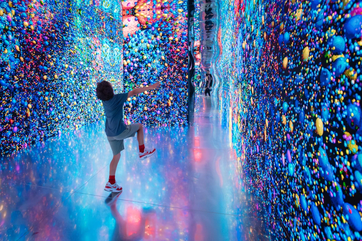 View of an exhibition space in Barcelona. A young man walks through a room. The walls seem to be animated and follow his movement.