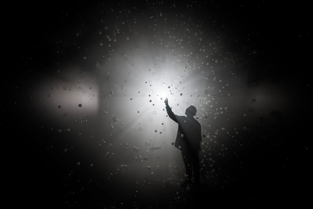 Black and white image. You can see the silhouette of a person illuminated by a spotlight. Small soap bubbles are flying in the air.