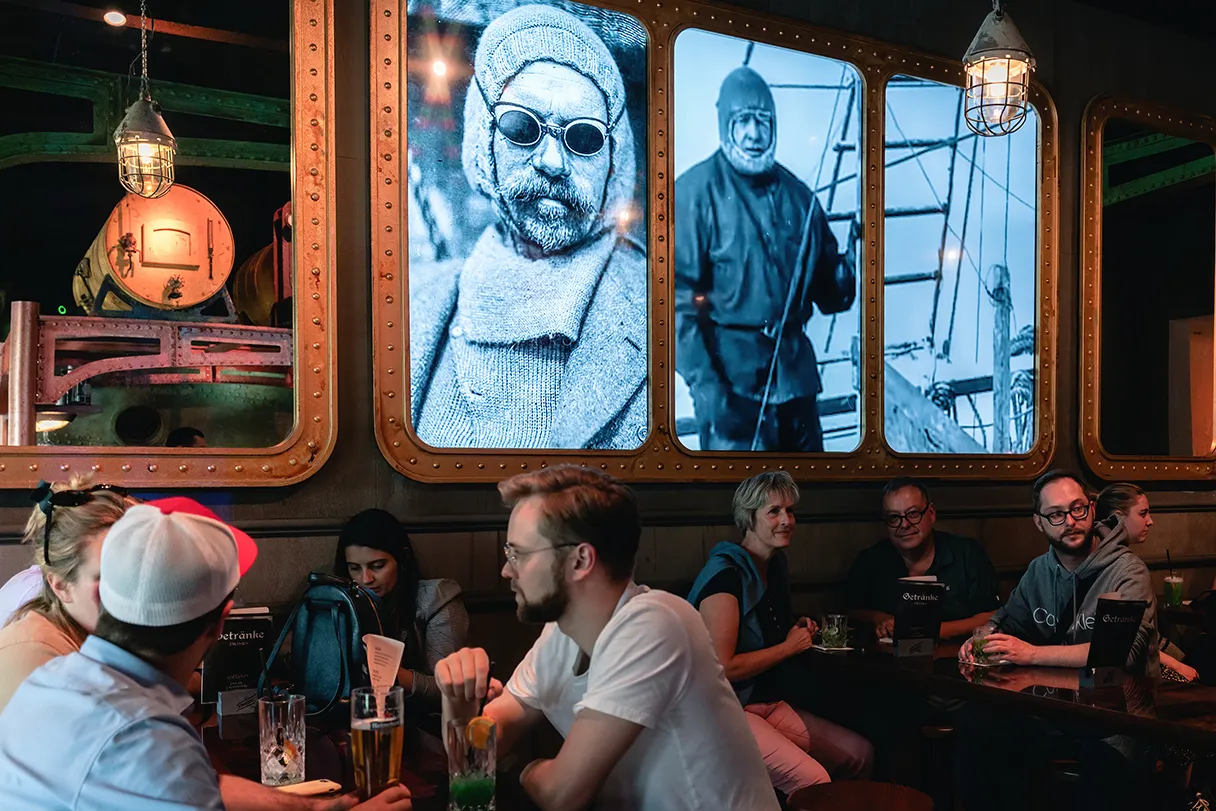Berlin Icebar, Gäste sitzen an Tischen, im Hintergrund große Bilder von Polarexpediteuren