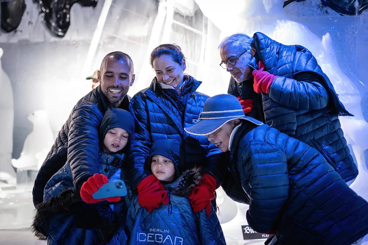 Berlin Icebar, Gruppe Erwachsenen und Kinder machen ein Gruppenfoto in der Icebar, im Hintergrund sind Eisskulpturen