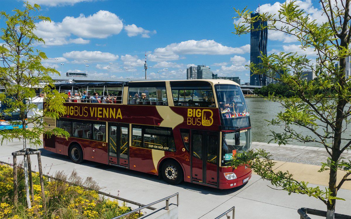 Big Bus Tours Vienna, bordeauxfarbener Sightseeingbus steht an der Donau