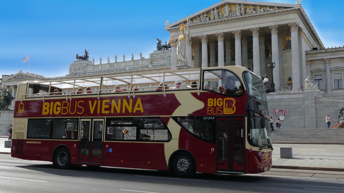 Big Bus Tours Vienna, bordeauxfarbener Sightseeingbus steht vor dem Parlament in Wien