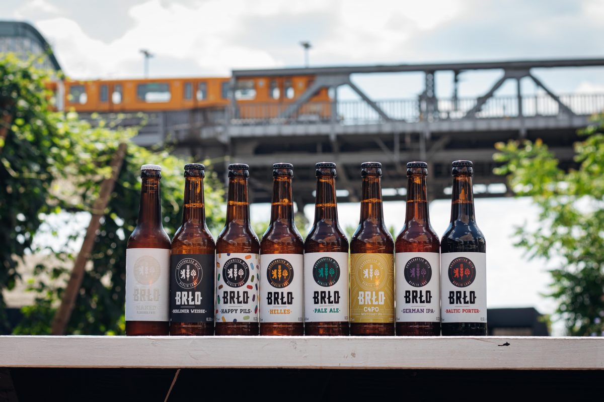 BRLO, verschiedenen braune Bierflaschen stehen nebeneinander aufgereiht, im Hintergrund für die U-Bahn über die Brücke am Gleisdreieck