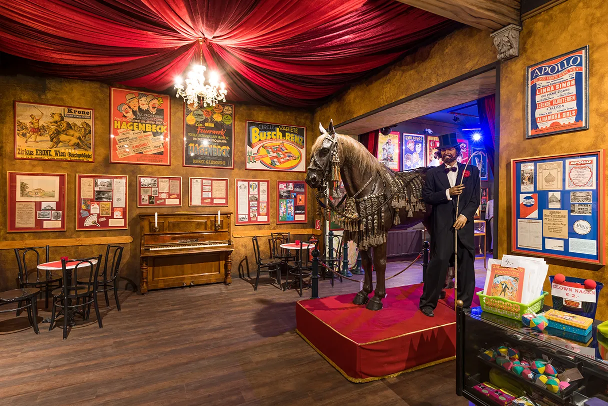 Circus & Clownmuseum Wien, Innenbereich des Museums, viele Ausstellungsstücke stehen im Raum, unter anderem ein braunes Pferd