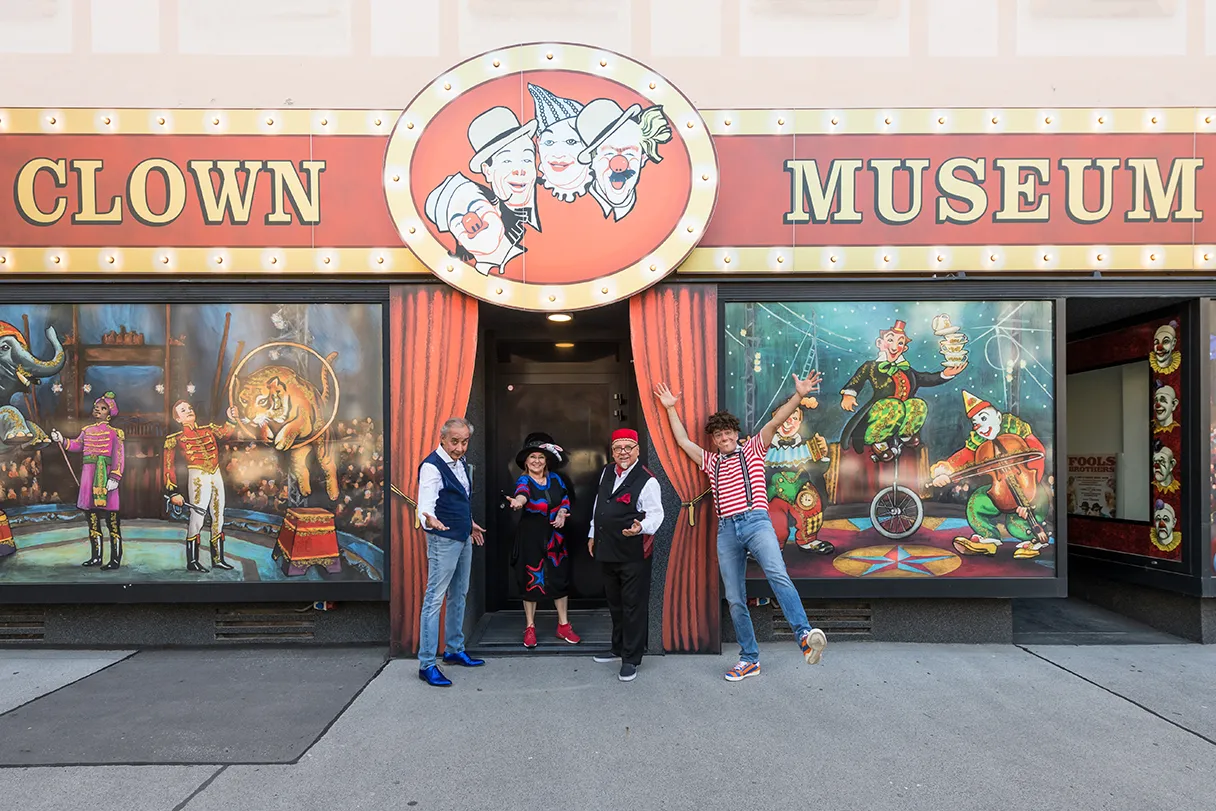 Circus & Clownmuseum Wien, Außenansicht, vier Personen stehen in bunten Kostümen vorm Eingangsbereich