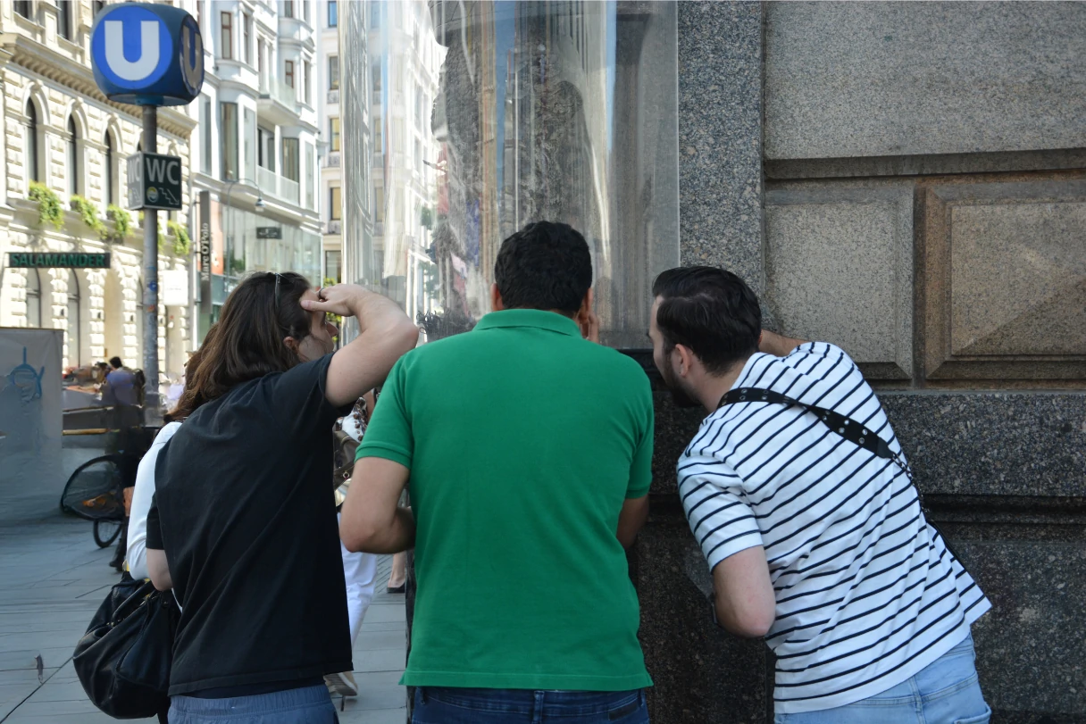 CityRiddler, vier Touristen stehen in Wien und gucken sich etwas an einem Haus an, was hinter einer Glaswand steht