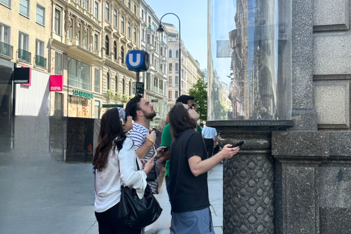 CityRiddler, vier Touristen stehen vor einer Hauswand und schauen sich etwas hinter einem Glas an