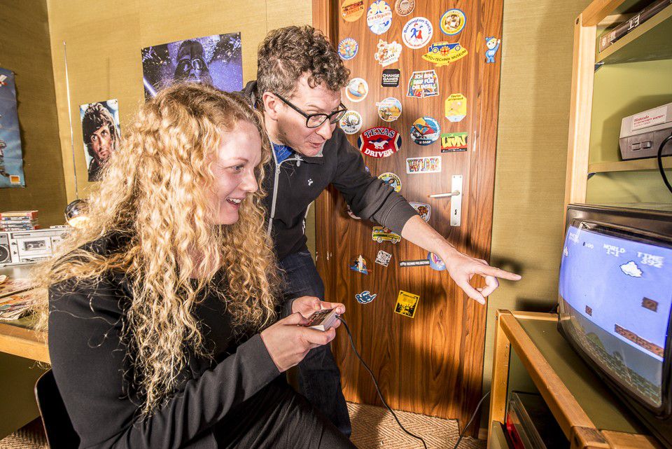 Computerspielemuseum, eine blonde Frau spielt am Fernseher Mario & Luigi, Umgebung ist wie ein Kinderzimmer gestaltet