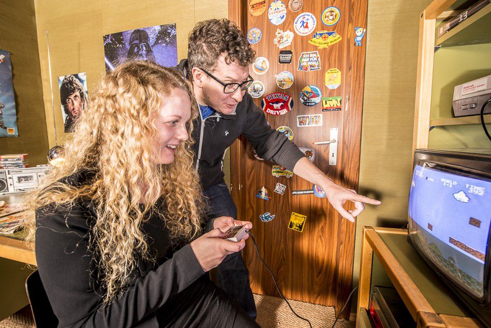 Computer games museum, blonde woman playing Mario & Luigi on TV, environment is designed like a child's room