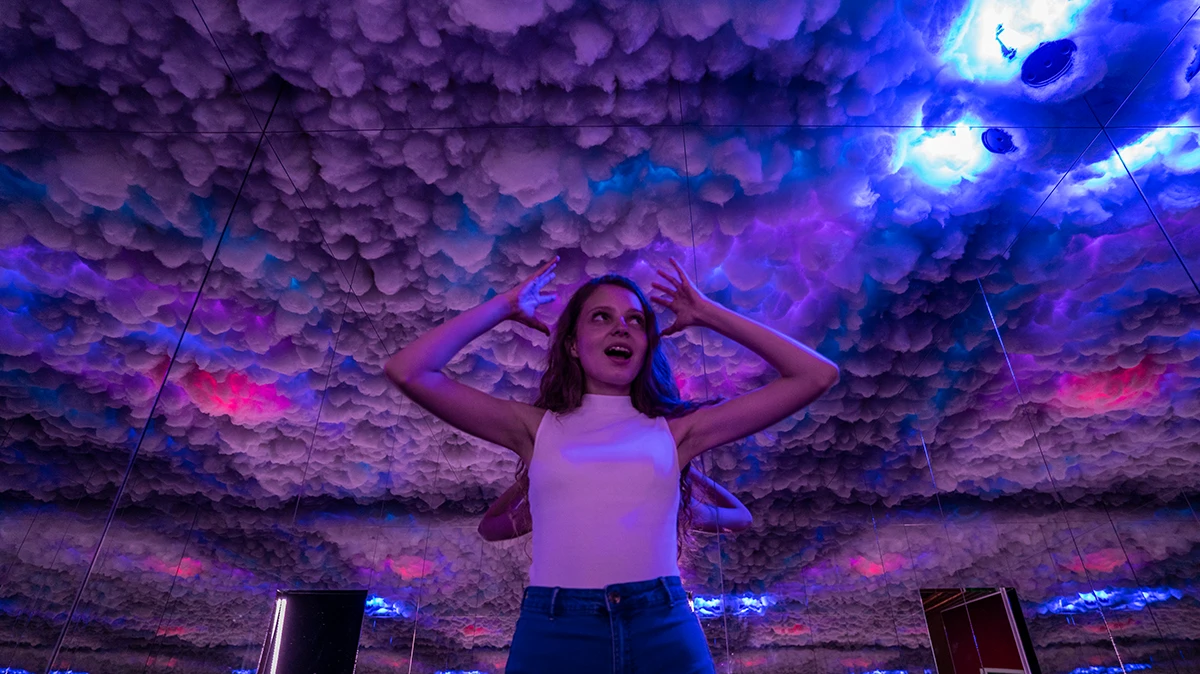 DeJa Vu Museum, junge Frau steht im Gewitterraum, Wolken über ihrem Kopf, blau-lila-Licht