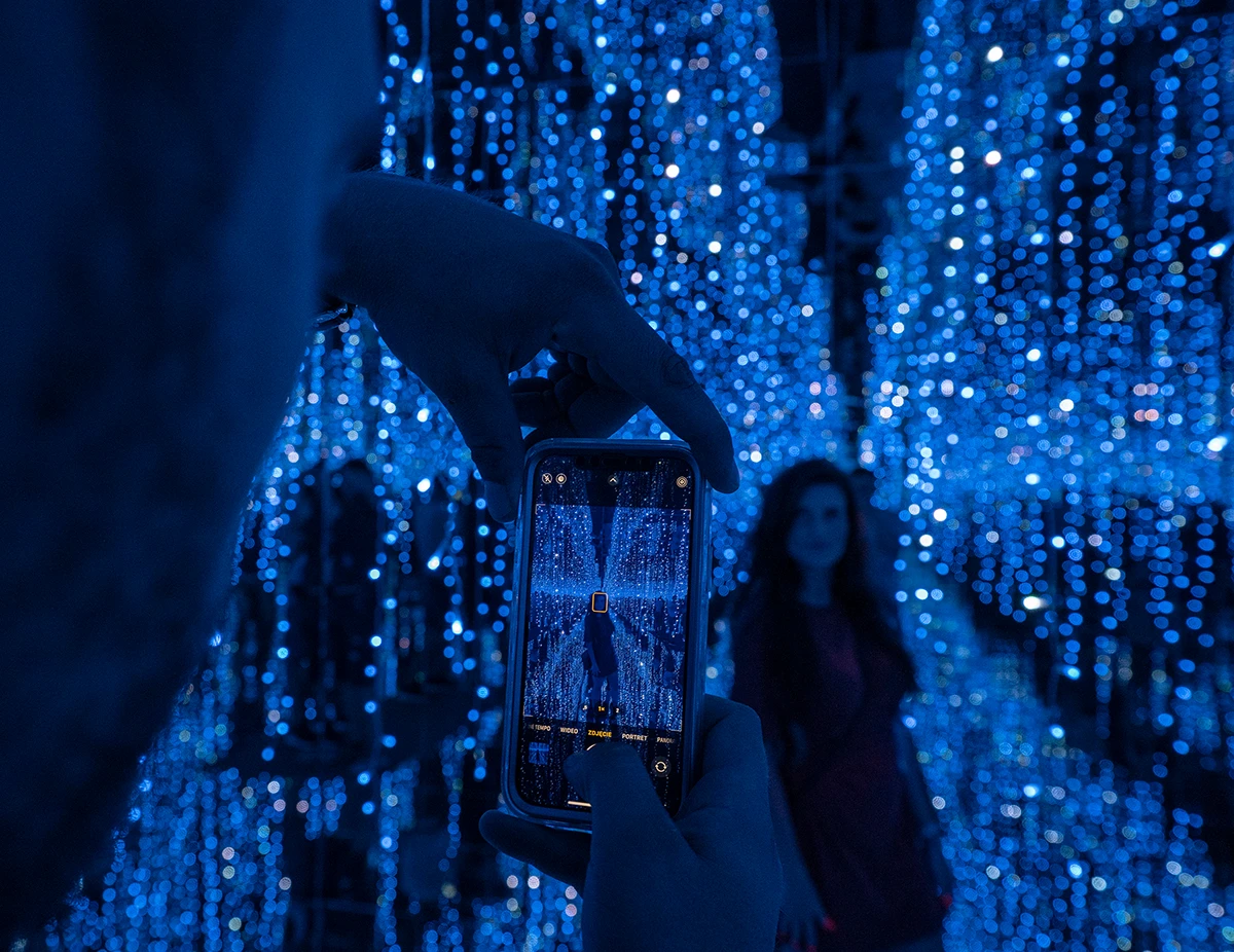 DeJa Vu Museum, ein Mann fotografiert eine Frau mit seinem Handy, blaues Licht und überall sind kleine Lichterketten