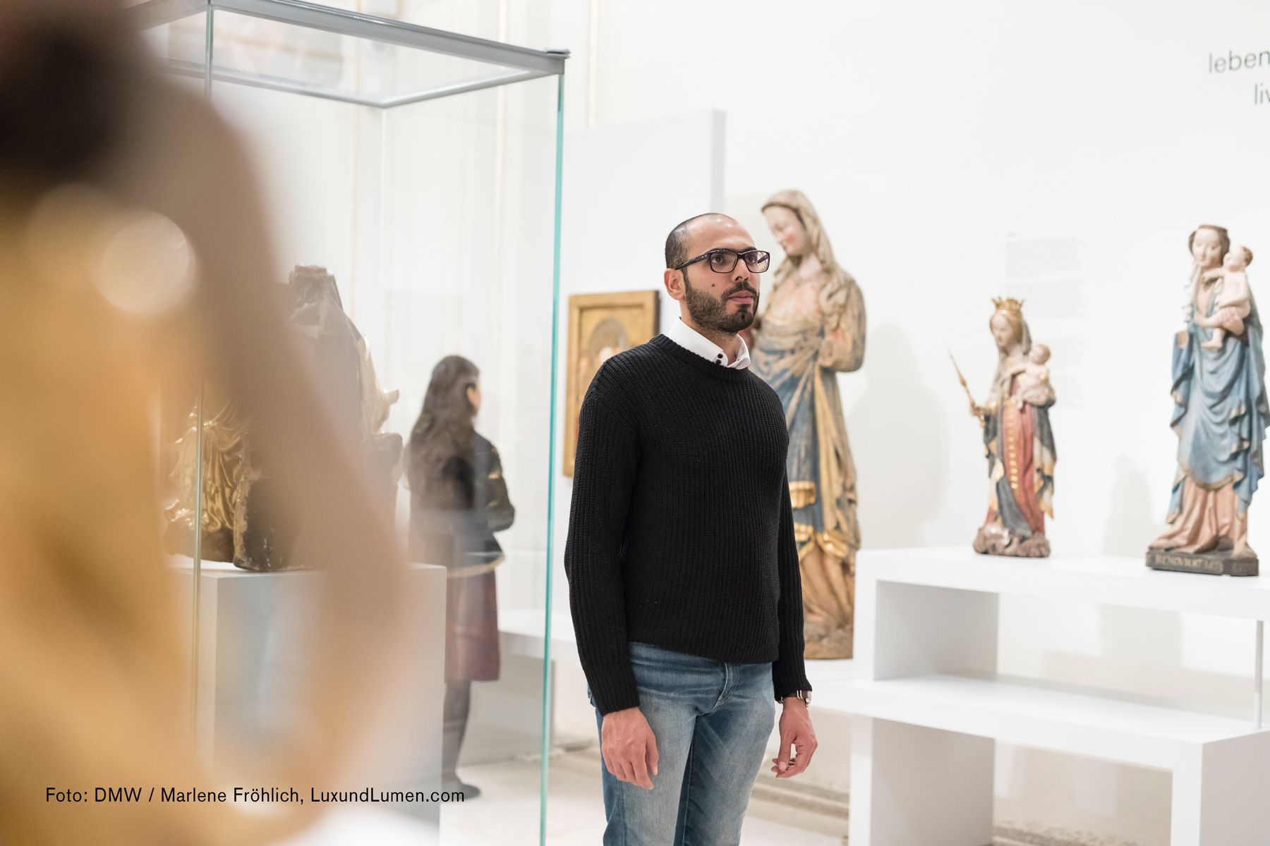 Dom Museum Wien, Mann mit schwarzer Brille und Pulli schaut sich die verschiedenen Marien Skultpuren an