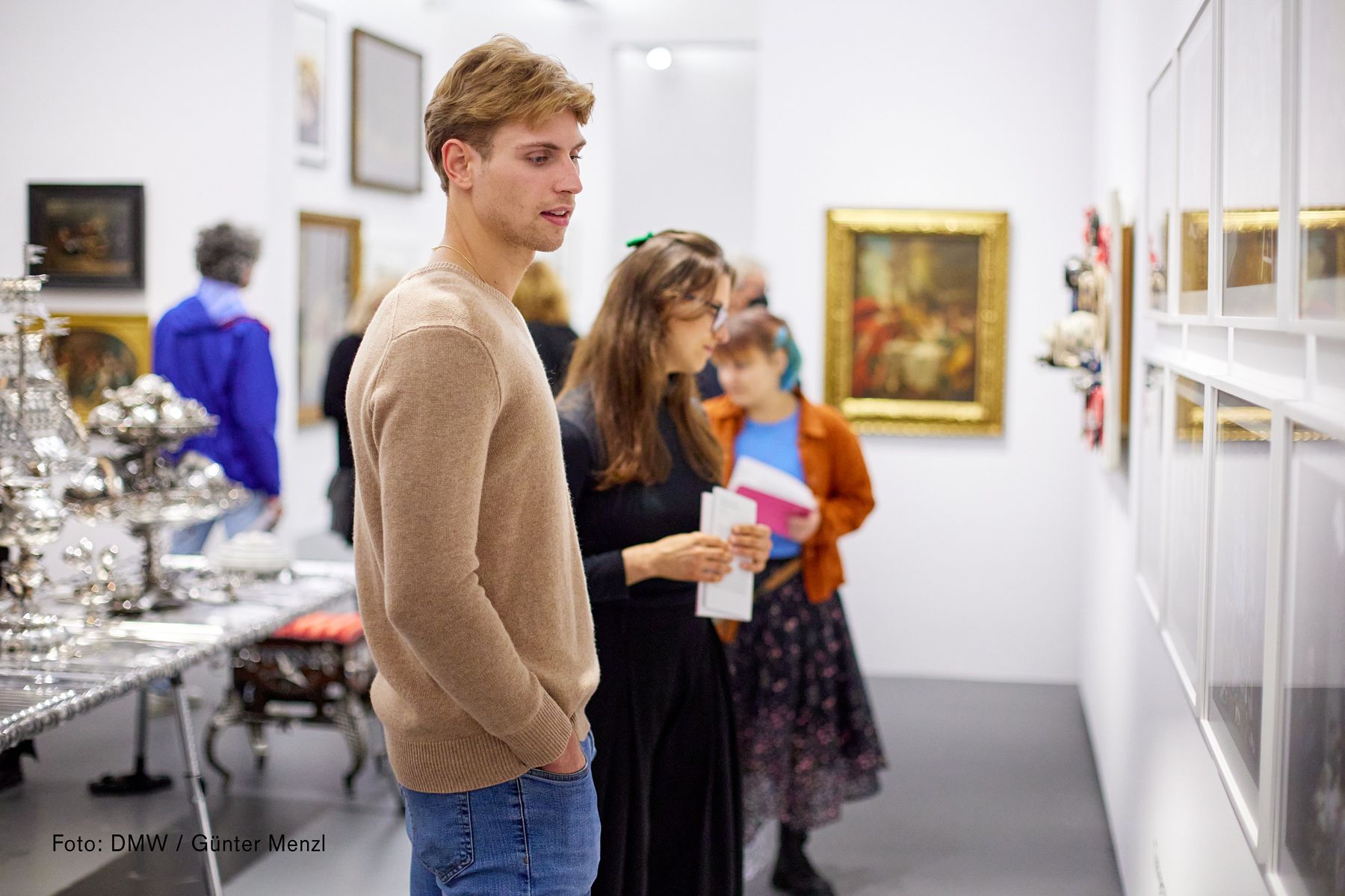 Dom Museum Wien, Gäste schauen sich die Exponate an der Wand an. Im Vordergrund steht ein junger Mann mit beigem Pullover und Jeans.