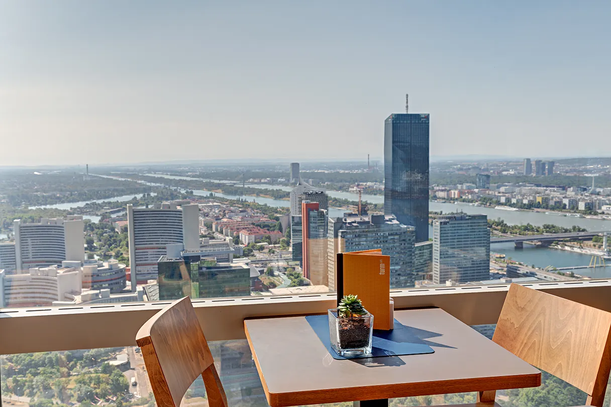 Donauturm. Turrmcafe. Tisch und zwei Stühle stehen am Panoramafenster. Gute Sicht nach draußen an einem sonnigen Tag.