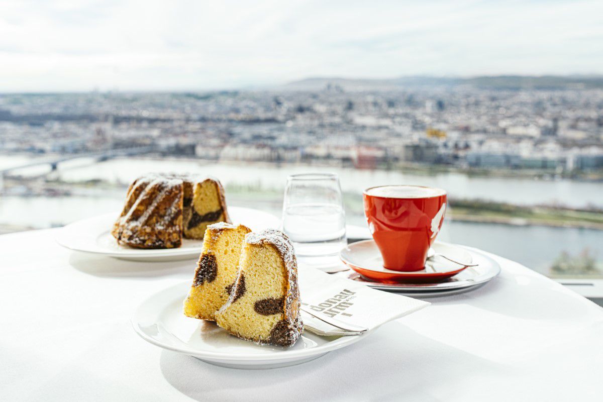 Donauturm, Turmcafé, auf einem weißen Tischen stehen zwei Teller mit Kuchen drauf, rote Tasse mit Kaffe, Blick über Wien
