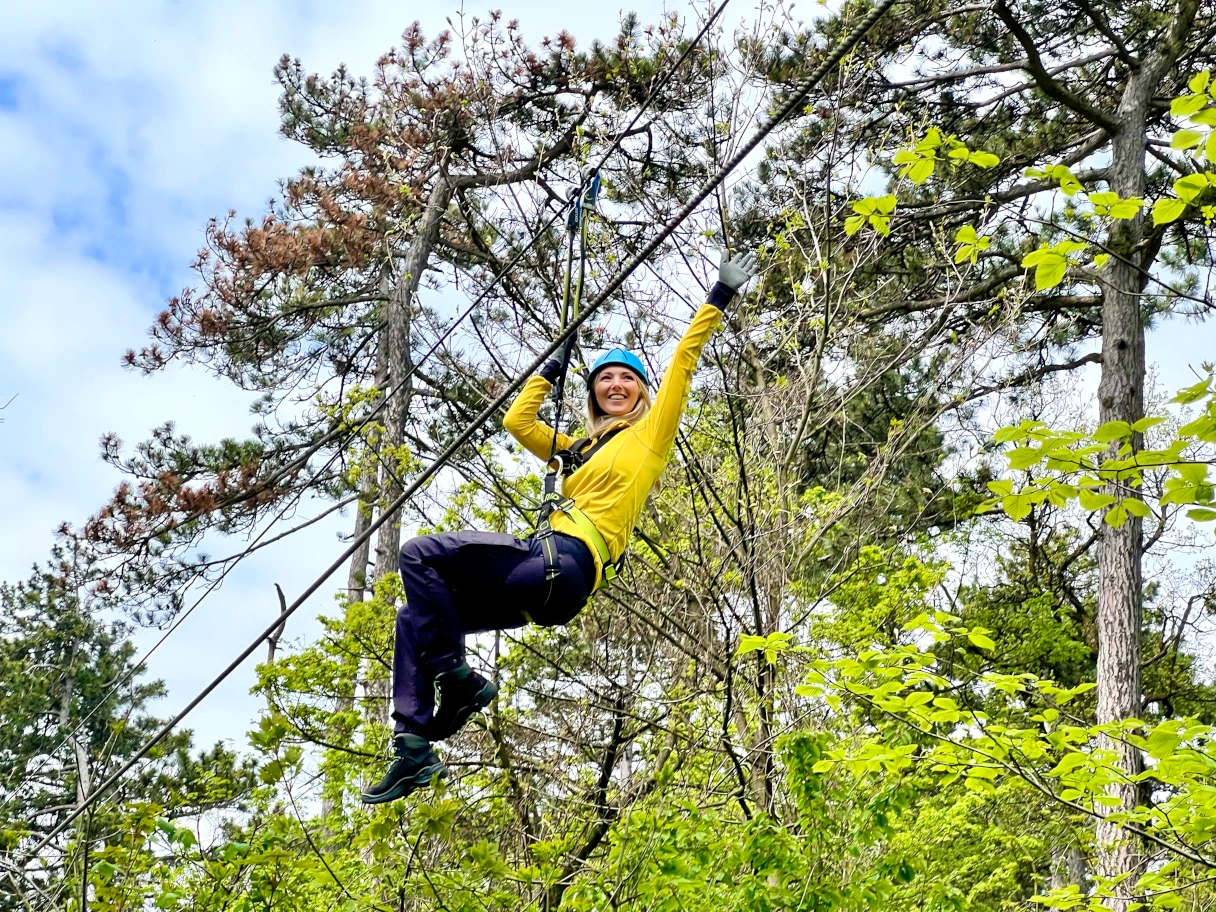 Frau in gelber Jacke hängt an einem Seil, mitten im Wald, in den Baumwipfeln